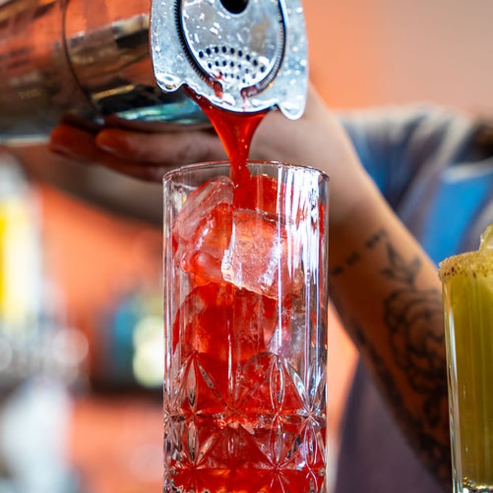 Red cocktail being poured from a shaker into a glass with ice at Mi Barrio Kitchen & Cocktails.